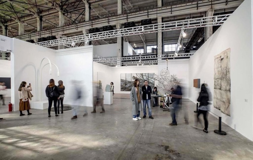 People walking through a contemporary art exhibition in a large industrial-style gallery space.