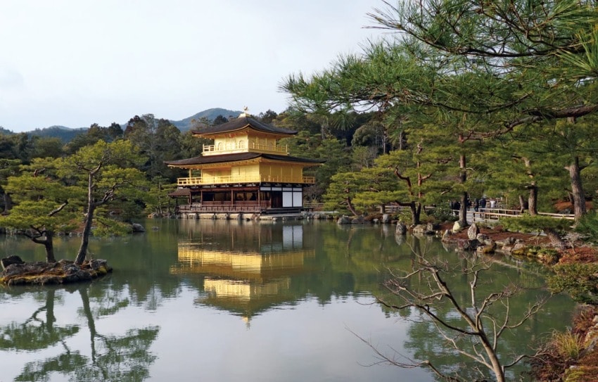 Golden Pavilion temple surrounded by trees, reflecting on a serene pond in Kyoto, Japan.