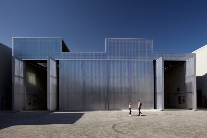Modern industrial building with large open doors, people walking nearby against clear blue sky.