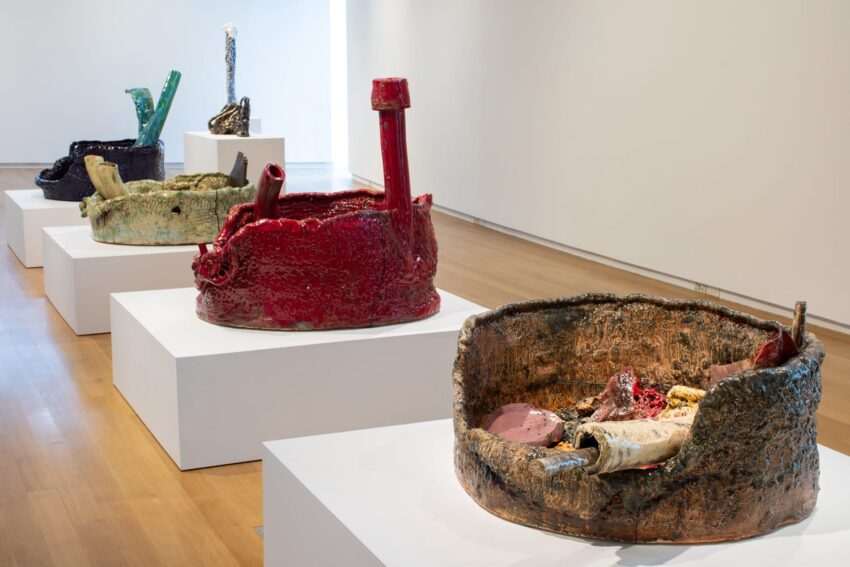 Colorful ceramic sculptures displayed on white pedestals in a modern gallery setting.