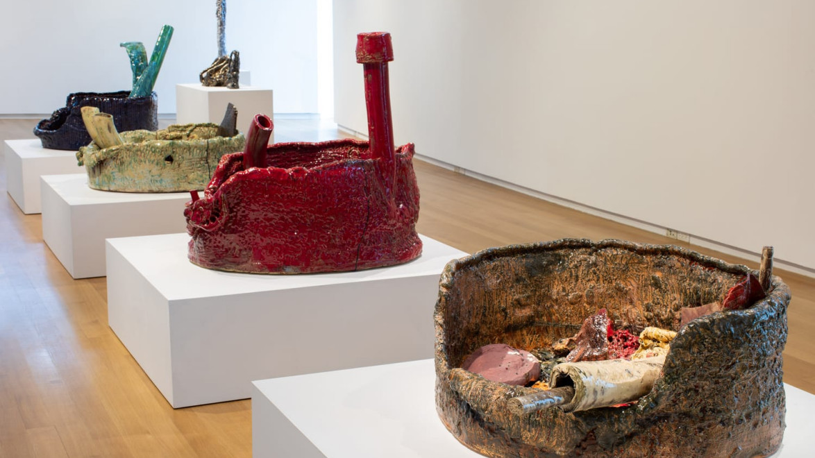 Colorful ceramic sculptures displayed on white pedestals in a modern gallery setting.