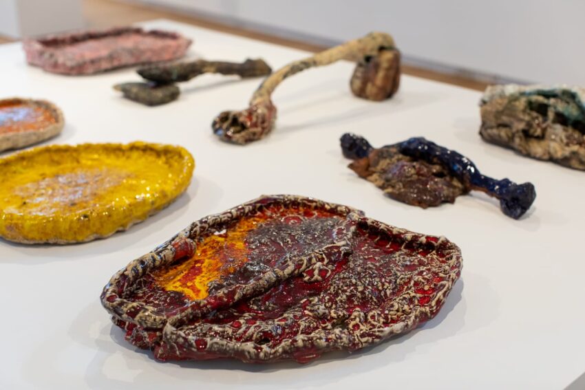 Various colorful, abstract ceramic sculptures displayed on a white table in an art gallery setting.