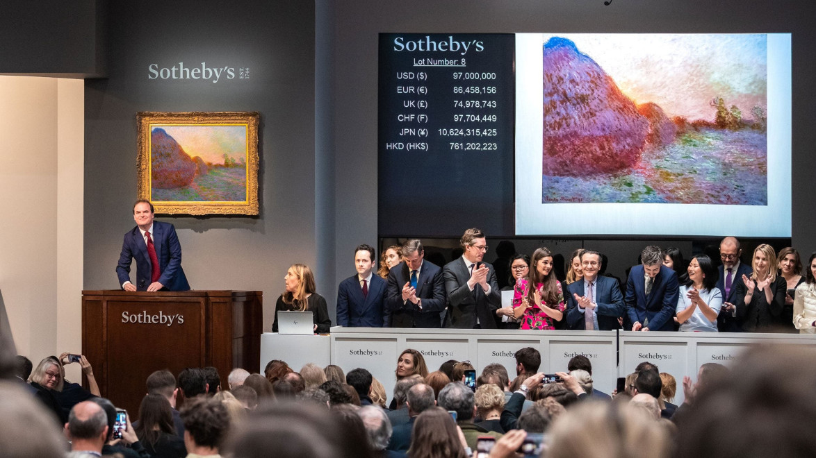 Auction at Sotheby's with auctioneer at podium, painting on display, and audience clapping.