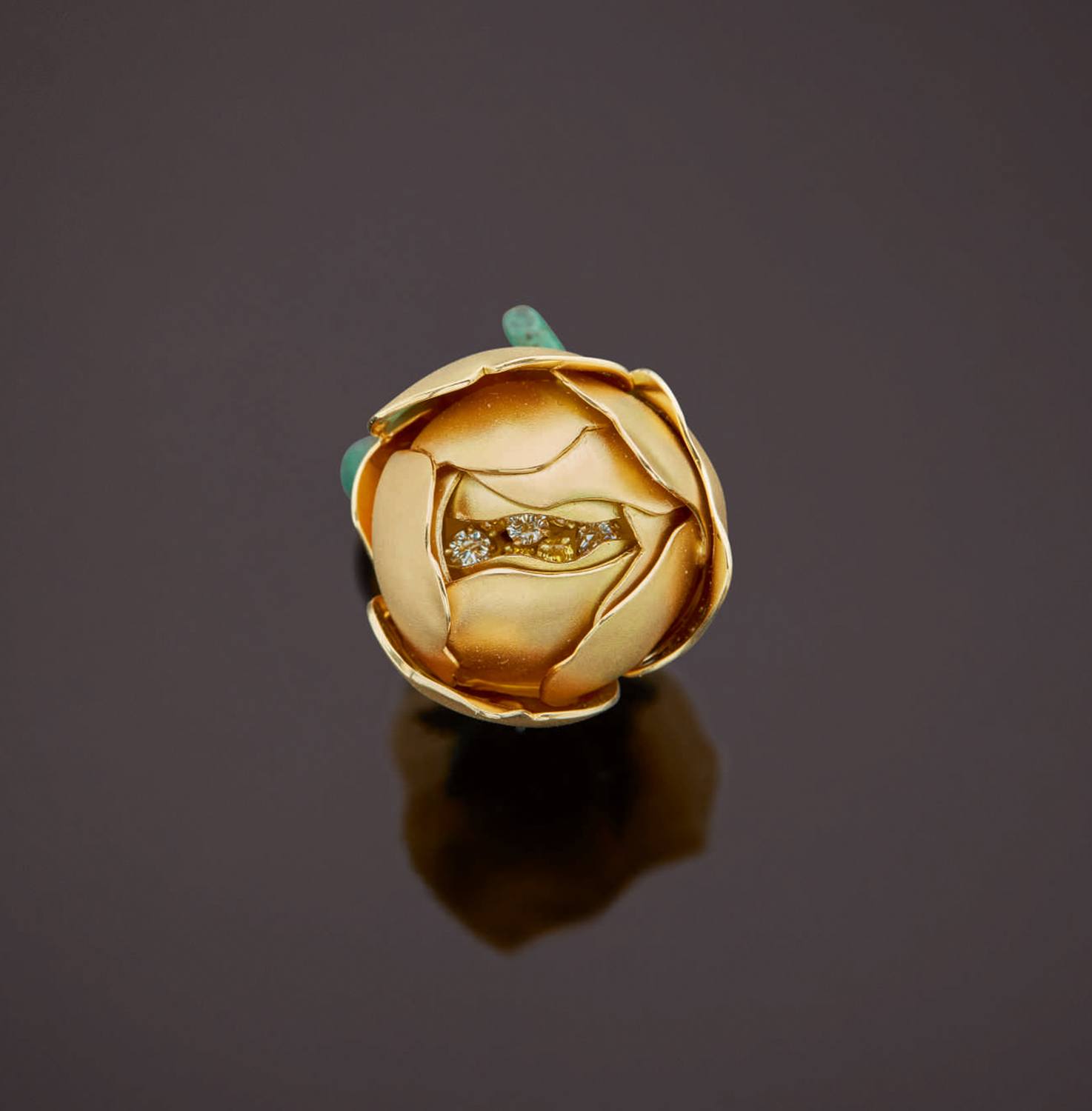 Gold flower-shaped ring with diamond center on dark reflective surface.