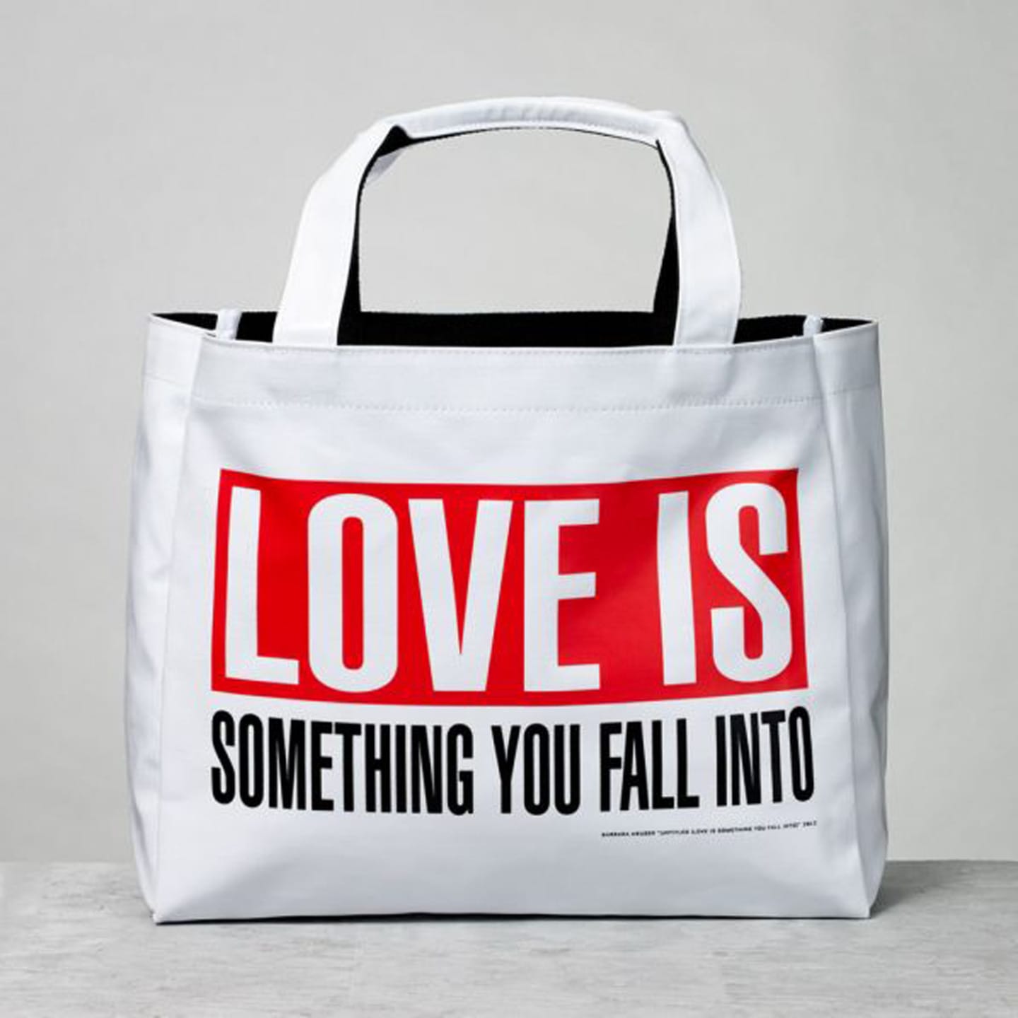 White tote bag with "Love is something you fall into" printed in bold red and black letters on a white surface.