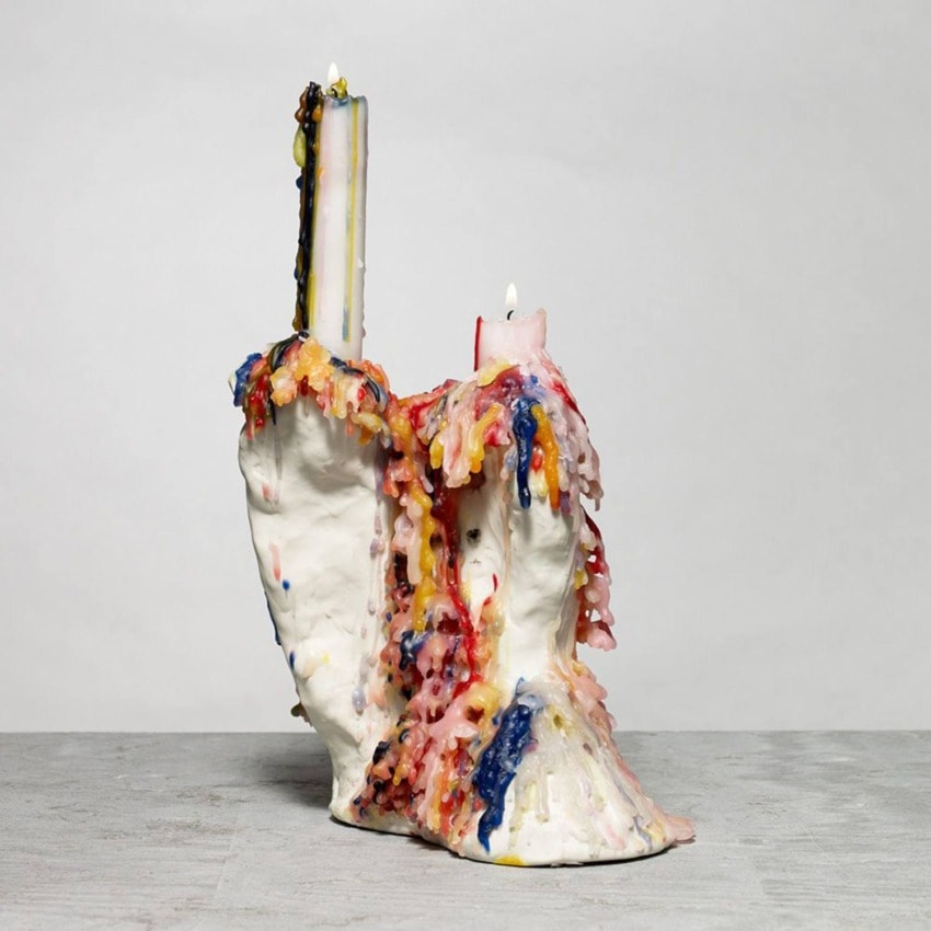 Colorful melted candle wax sculpture on a gray surface with various drippings in red, blue, and yellow.