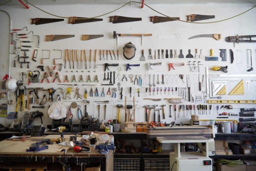 Organized woodworking tools hanging on a workshop wall with various saws, hammers, and other equipment neatly displayed.