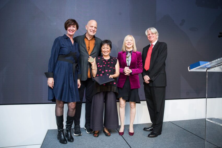 Five people standing together, dressed formally, smiling at a presentation or event.