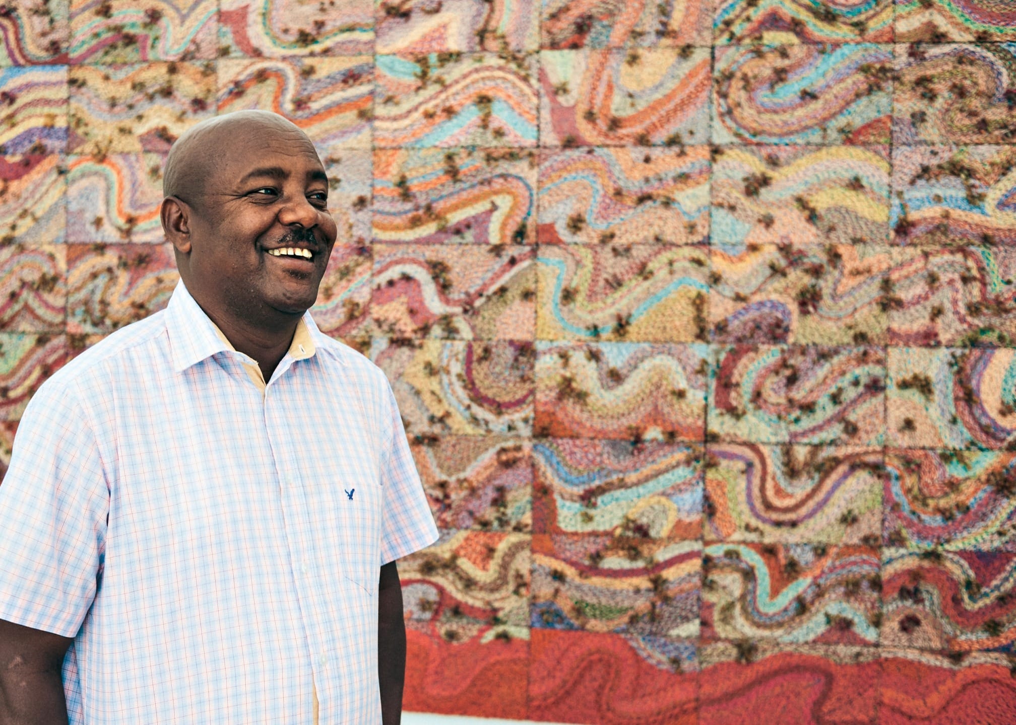Man smiling in front of a vibrant, colorful abstract mural with a checkered shirt.