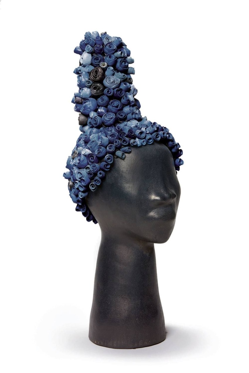 Mannequin head wearing a tall, intricate blue and black rolled paper headpiece on white background.