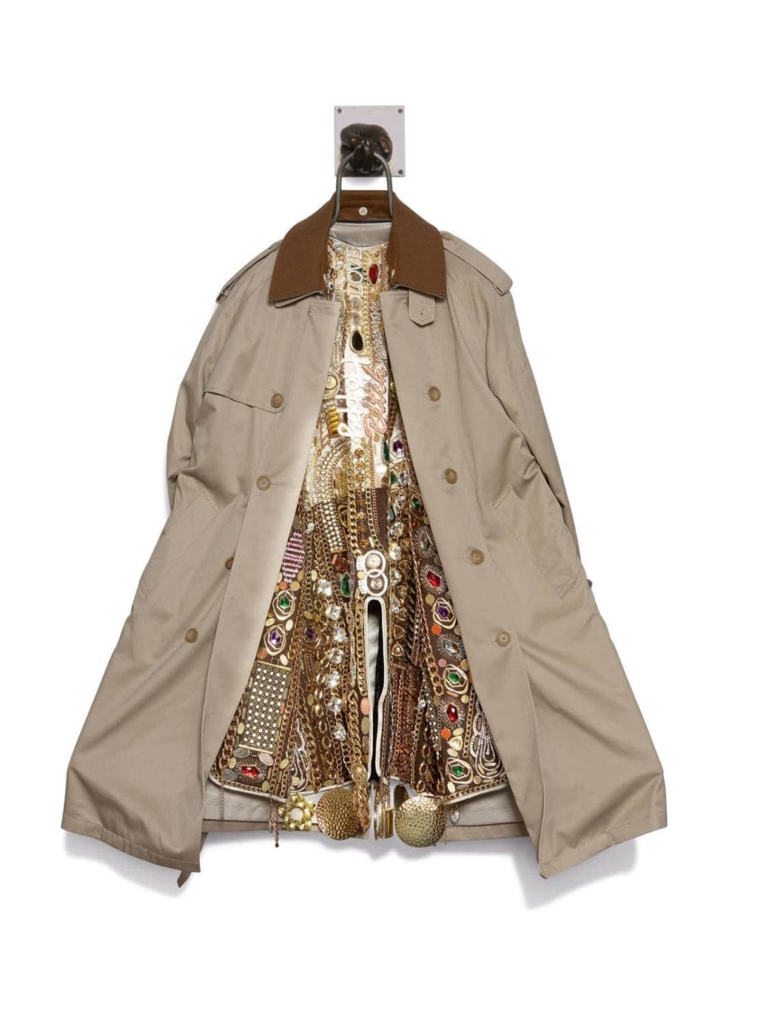 Beige trench coat with a richly embroidered, colorful metallic interior hanging on a wall hook.