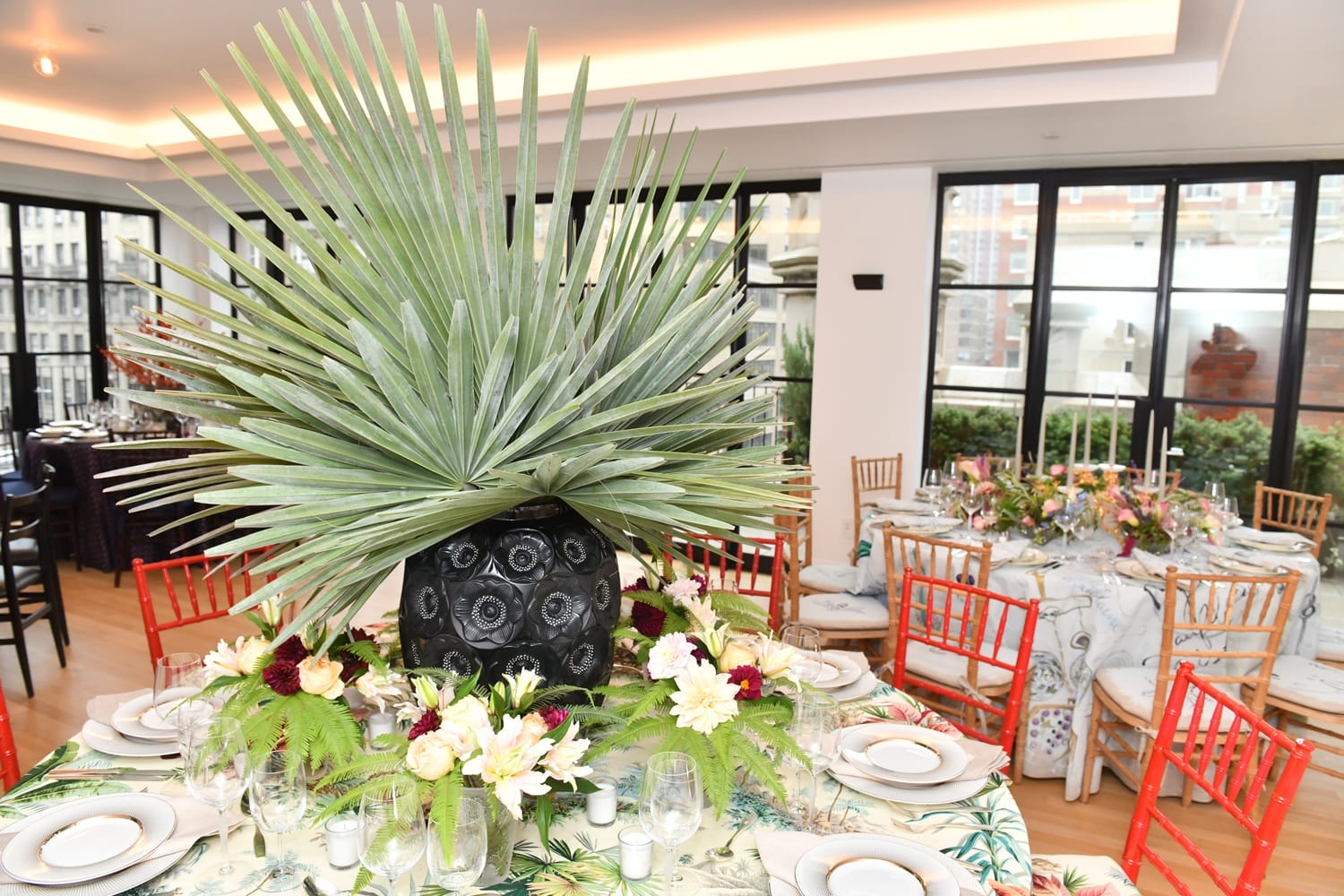 Elegant dining setup with palm centerpiece, floral accents, and colorful chairs in a bright, modern venue.