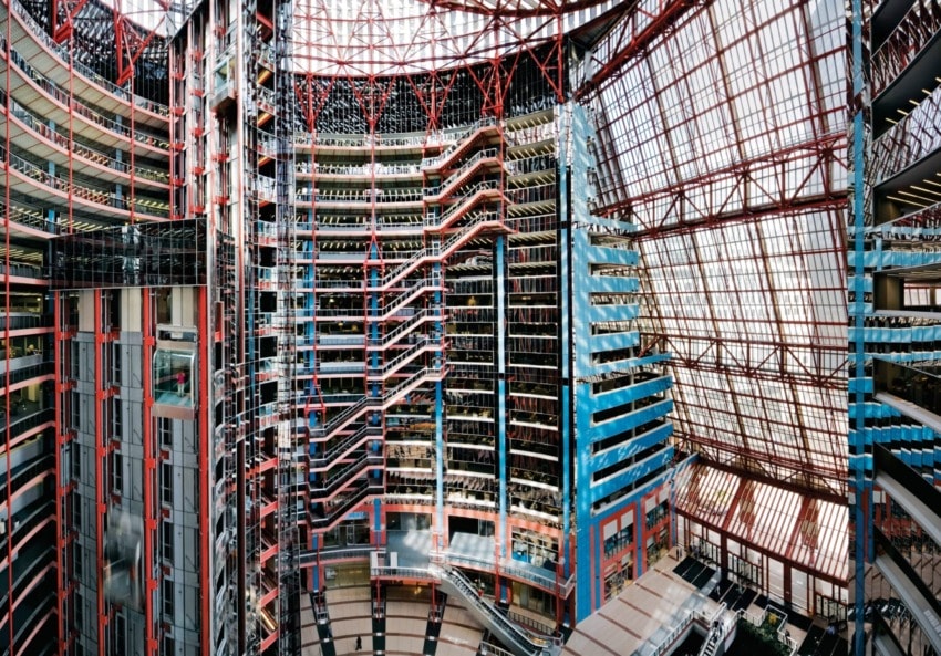 Interior of a modern, spacious atrium with multiple levels, glass ceilings, and colorful architectural elements.