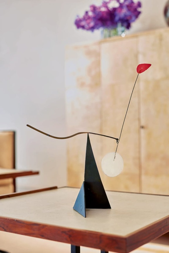 Modern abstract sculpture on a wooden table with a geometric design and a red leaf-like shape on a thin wire.