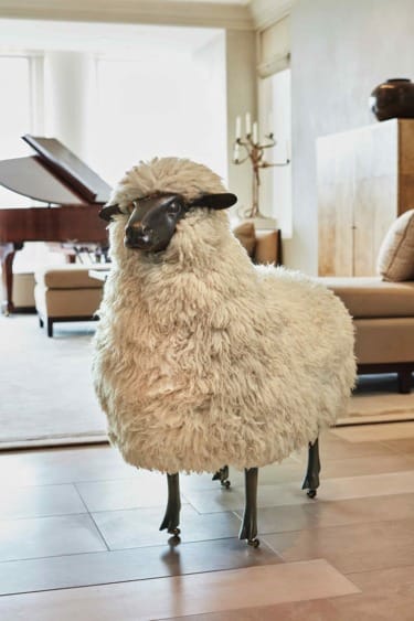 Sheep-shaped sculpture with woolly texture stands in a living room near a piano.