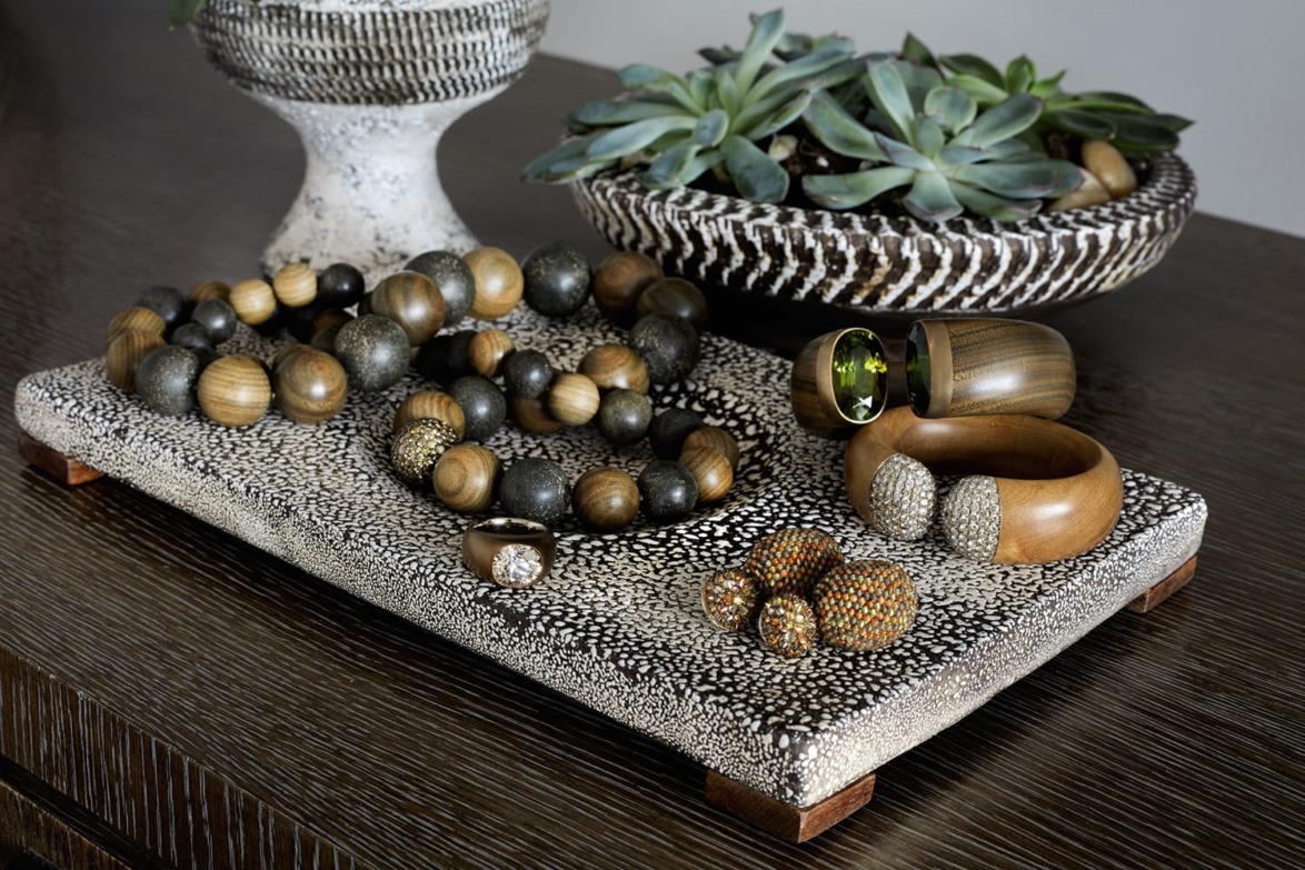 Display of wooden jewelry and succulent plants on a textured tray and table.