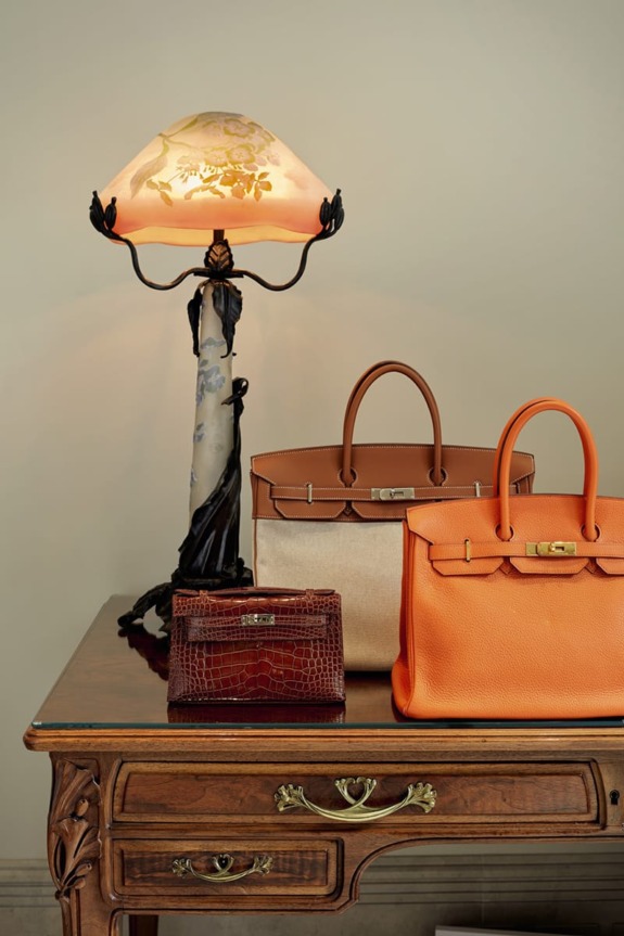Vintage table with a decorative lamp and three luxury handbags, including brown and orange styles, elegantly displayed.