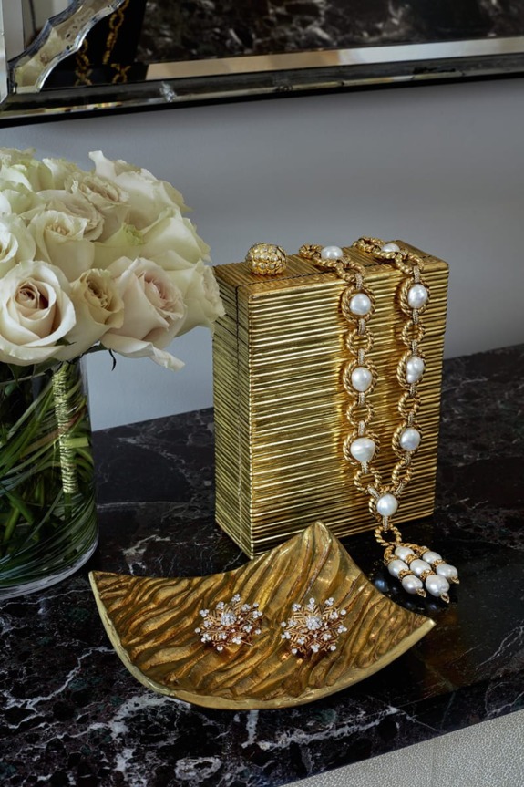 Elegant jewelry display with gold box and pearl necklace next to a vase of white roses on a marble surface.