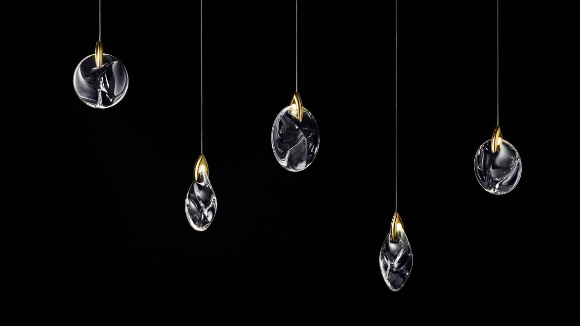 Five abstract pendants with glass and gold accents hanging against a black background.