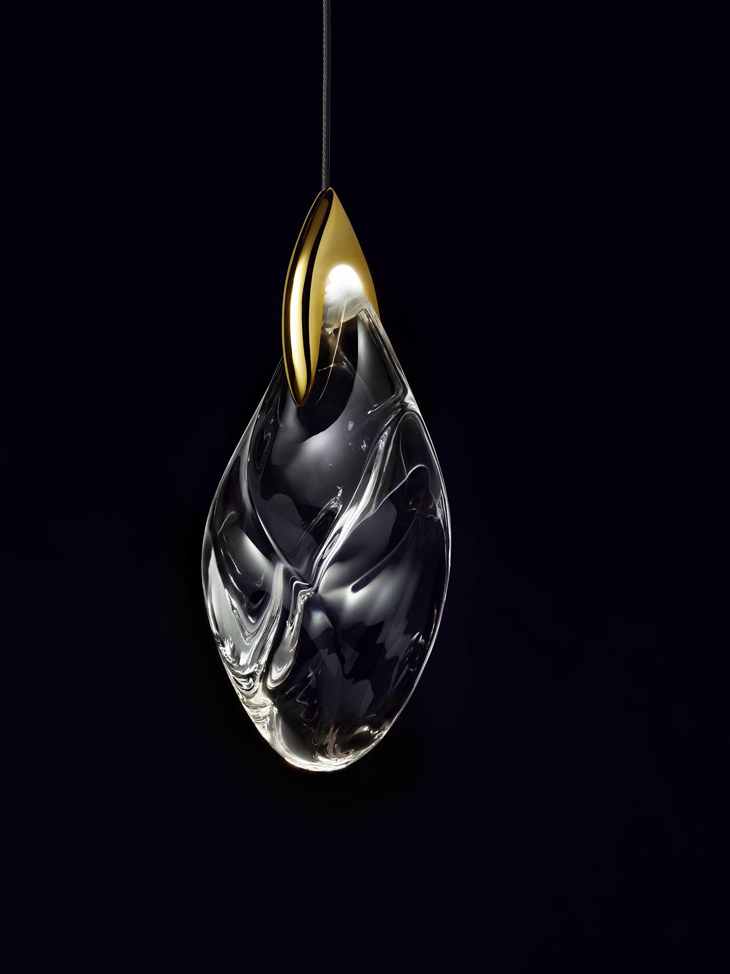 Elegant glass teardrop pendant light with a gold accent on a dark background.
