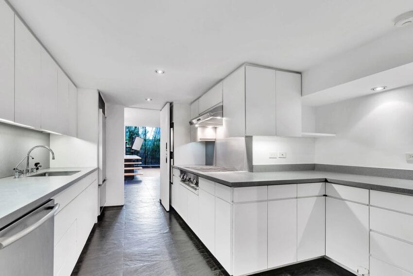 Modern kitchen with white cabinets, stainless steel appliances, and slate flooring, leading to a dining area with natural light.