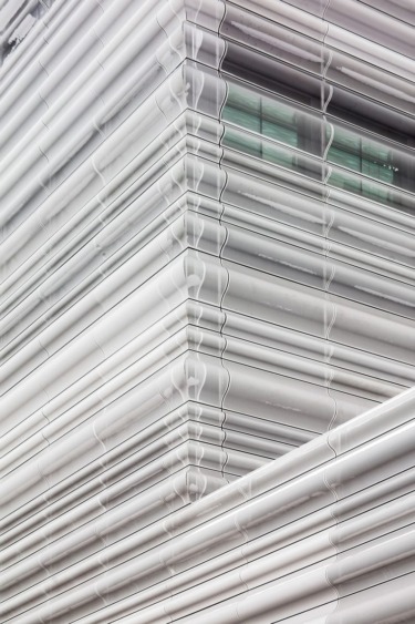 Close-up of a modern building facade featuring overlapping, metallic architectural panels with a geometric design.