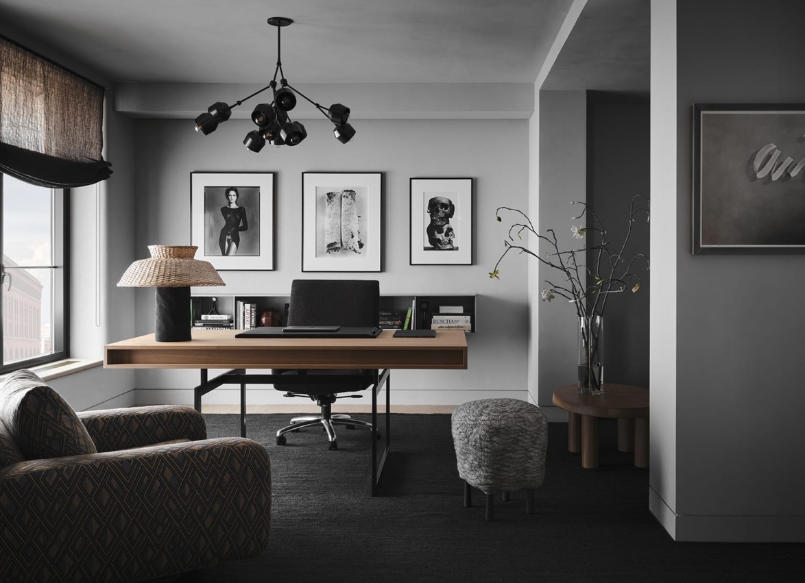 Modern home office with sleek black desk, stylish lighting, art on walls, and cozy seating.