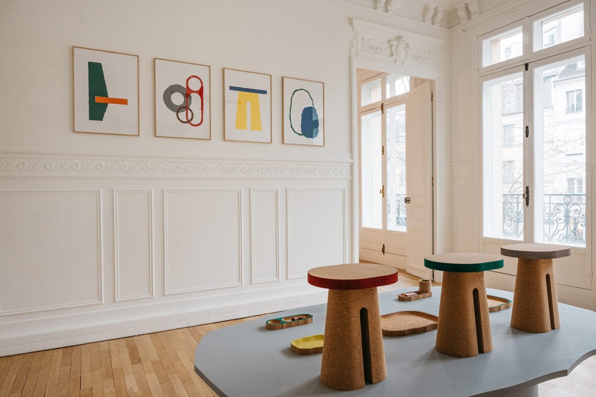 Room with abstract art on walls, wooden stools with colorful tops, large windows, and intricate wall molding.