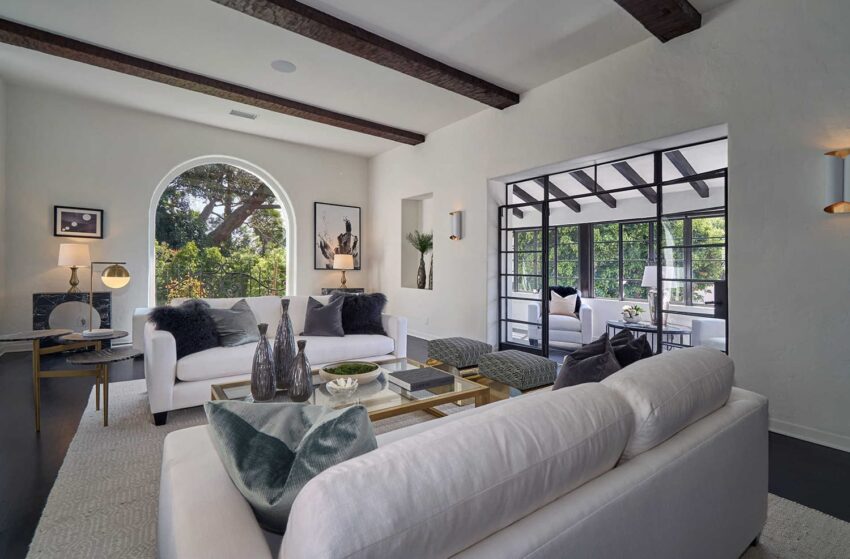 Modern living room with white sofas, decorative pillows, glass coffee table, and large windows with garden view.