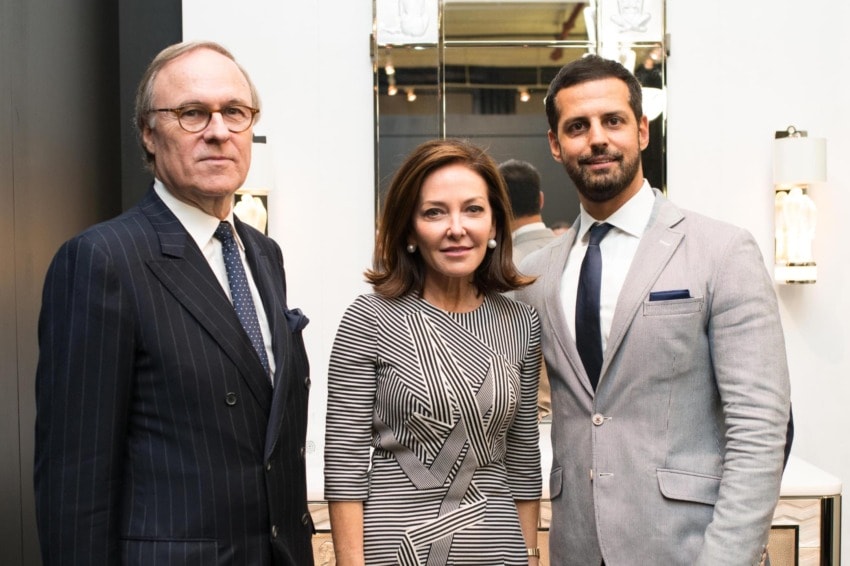 Three people in formal attire standing together indoors, smiling.