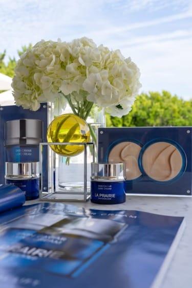 Skincare products arranged with a vase of white flowers outdoors on a table.