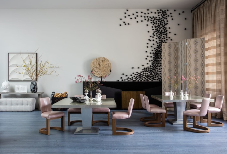 Modern dining room with pink chairs, metallic tables, abstract wall art, decorative items, and large window with curtains.