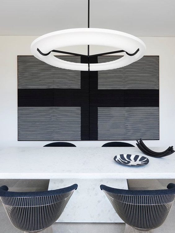 Modern dining room with a white circular chandelier, abstract wall art, marble table, and two sleek black chairs.