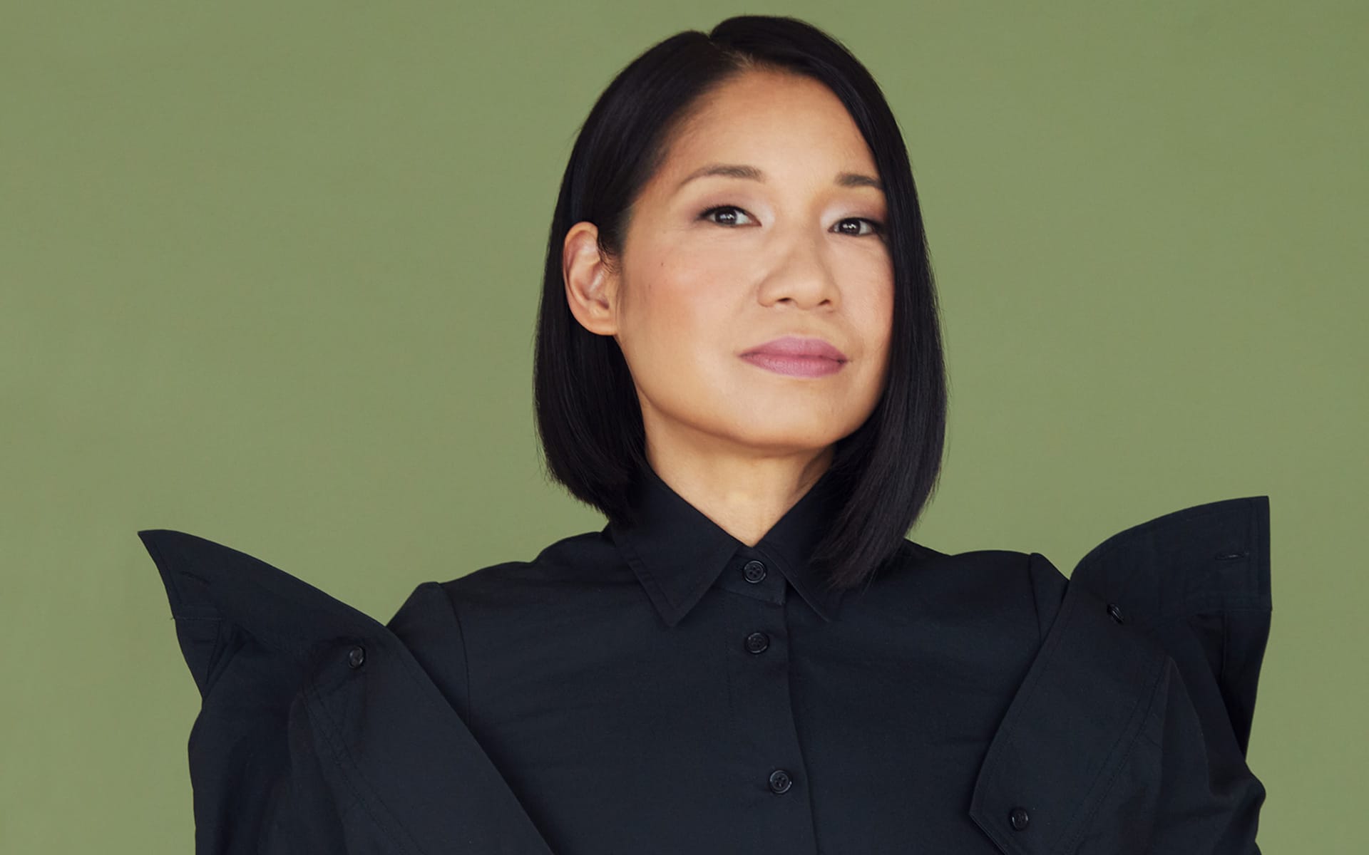 Person with short dark hair wearing a black shirt against a green background.
