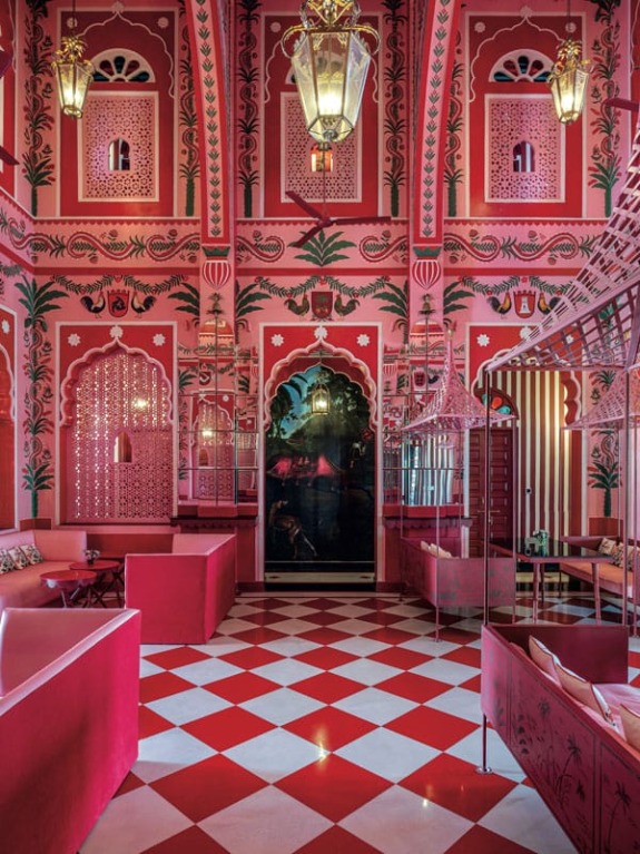 Vibrant pink and red interior with patterned walls, ornate arches, lanterns, and red checkered floor tiles.
