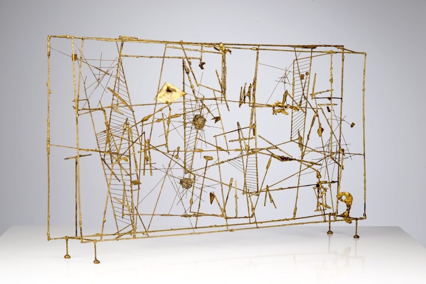 Abstract metal sculpture with interconnected wires and geometric shapes displayed on a white surface against a gray background.