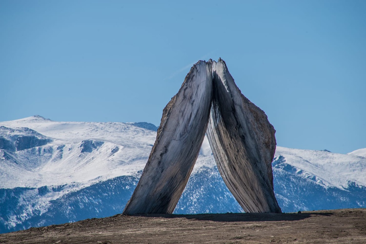 Large stone sculpture with mountain backdrop against clear blue sky.