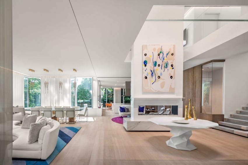 Modern open-plan living room with abstract art, light wood floors, white furniture, and large windows letting in natural light.