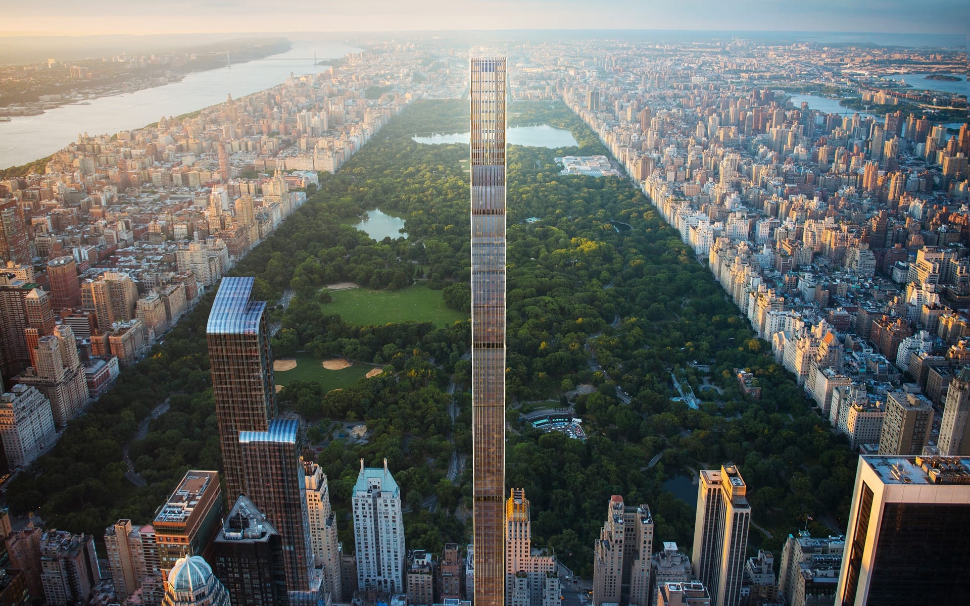 Aerial view of a tall skyscraper in front of Central Park surrounded by urban cityscape at sunset.