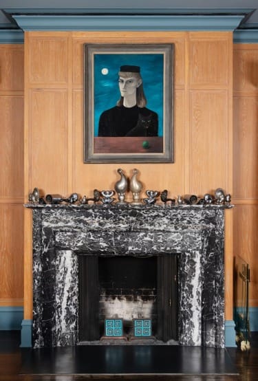 Fireplace with marble mantle, decorative pieces, and portrait painting on wood-paneled wall.
