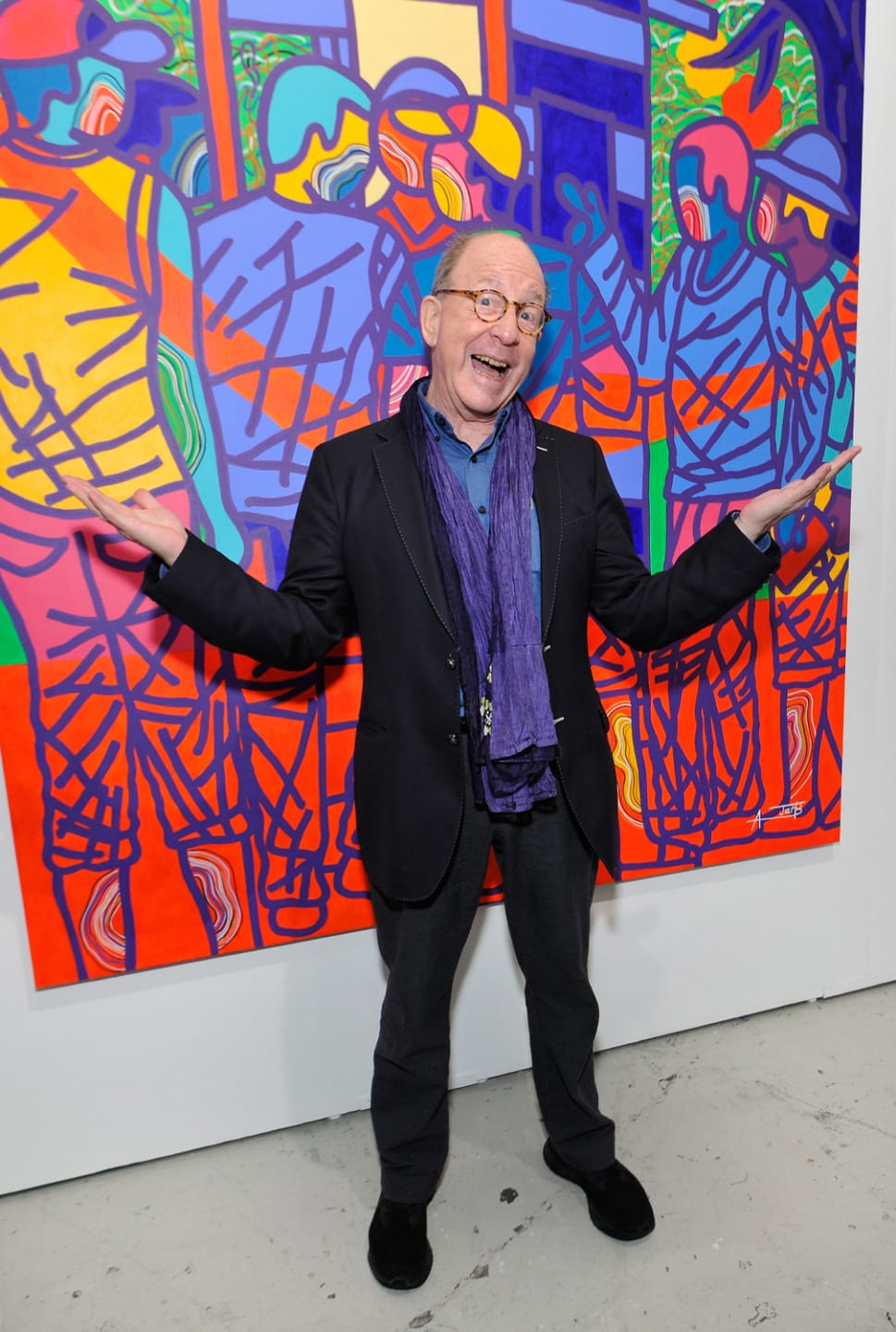 Celebratory man in front of colorful abstract mural with vibrant, geometric designs and multiple figures in the artwork.