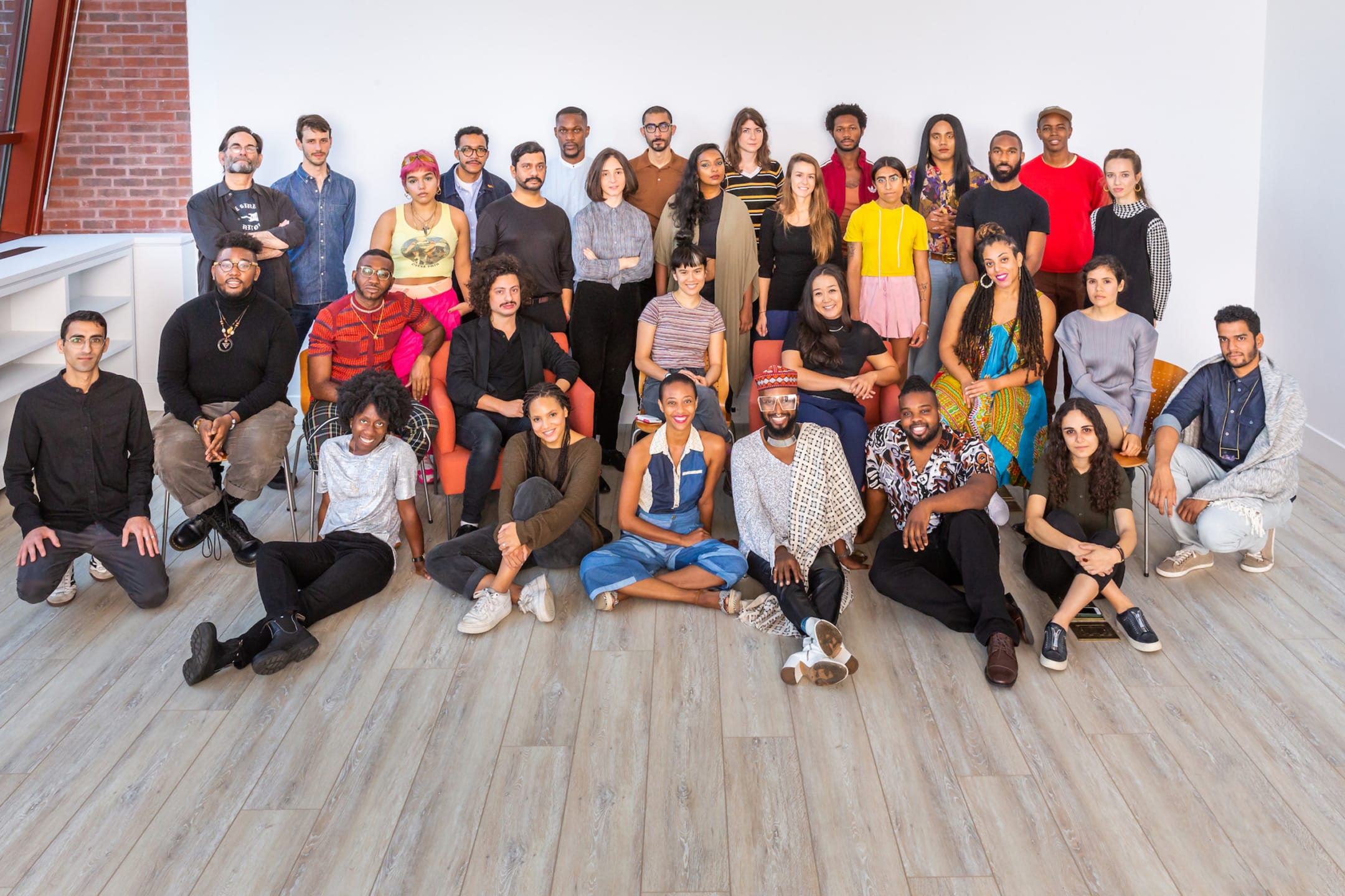 A diverse group of people posing together in a bright room with wooden flooring