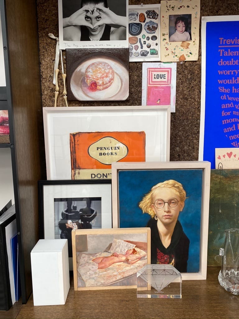 Artistic wall display with various framed photos, drawings, and prints featuring people, a sandwich, and geometric designs.