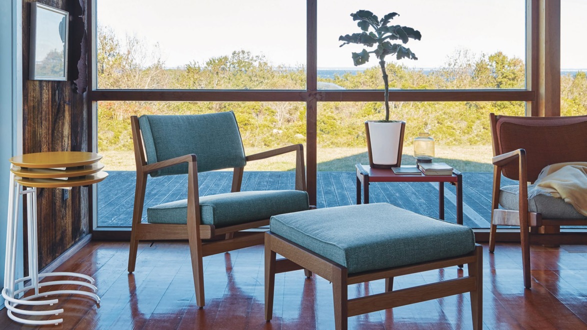 Modern living room with wooden furniture, green chair, ottoman, and a potted plant, overlooking a scenic outdoor view.