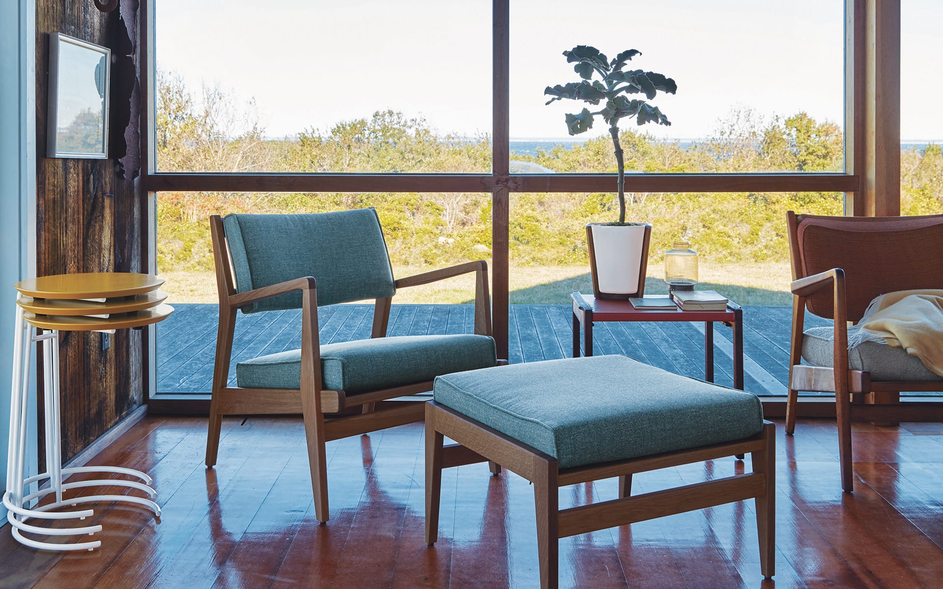 Modern living room with wooden furniture, green chair, ottoman, and a potted plant, overlooking a scenic outdoor view.