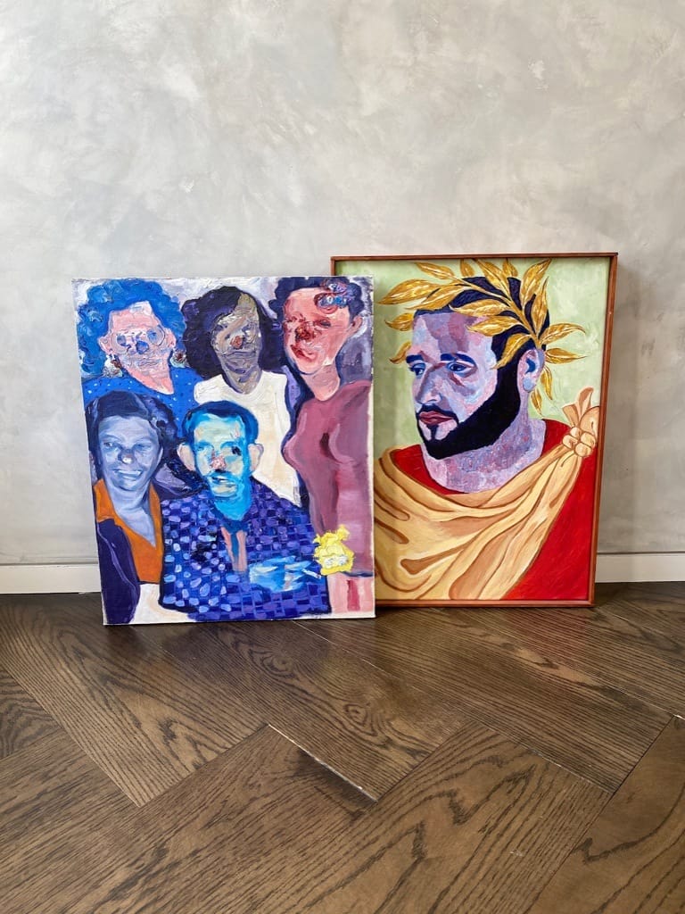 Two colorful paintings on wooden floor; one depicts a group of people and the other is a portrait with a laurel wreath.