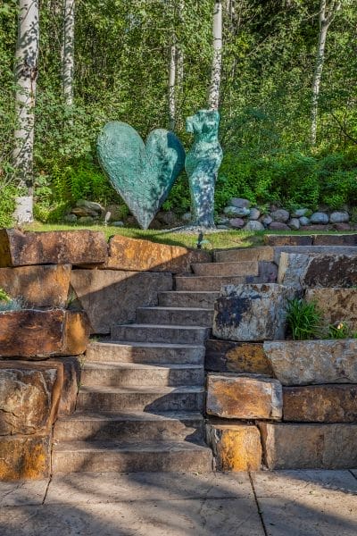Stone staircase leading to heart and abstract figure sculptures surrounded by trees and greenery.