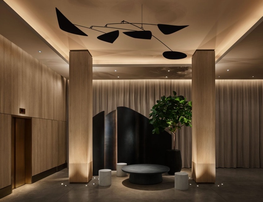 Modern lobby with abstract ceiling mobile, tall columns, a round coffee table, stools, and a potted plant.
