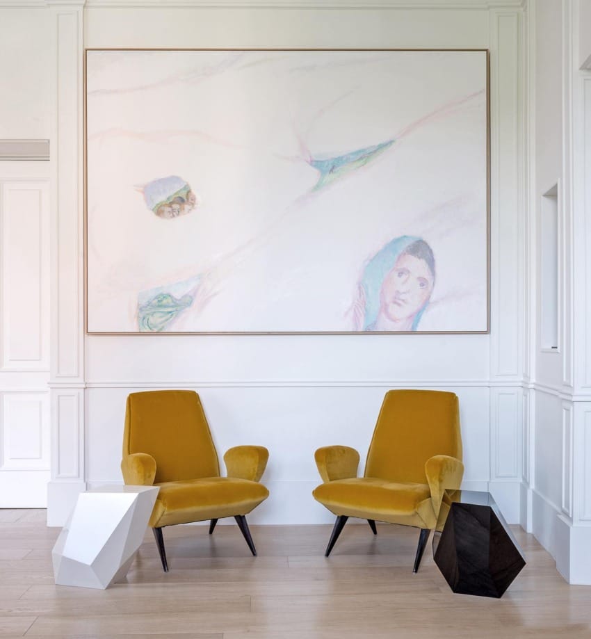 Two mustard yellow chairs in a modern art gallery setting with a large abstract painting on a white wall in the background.