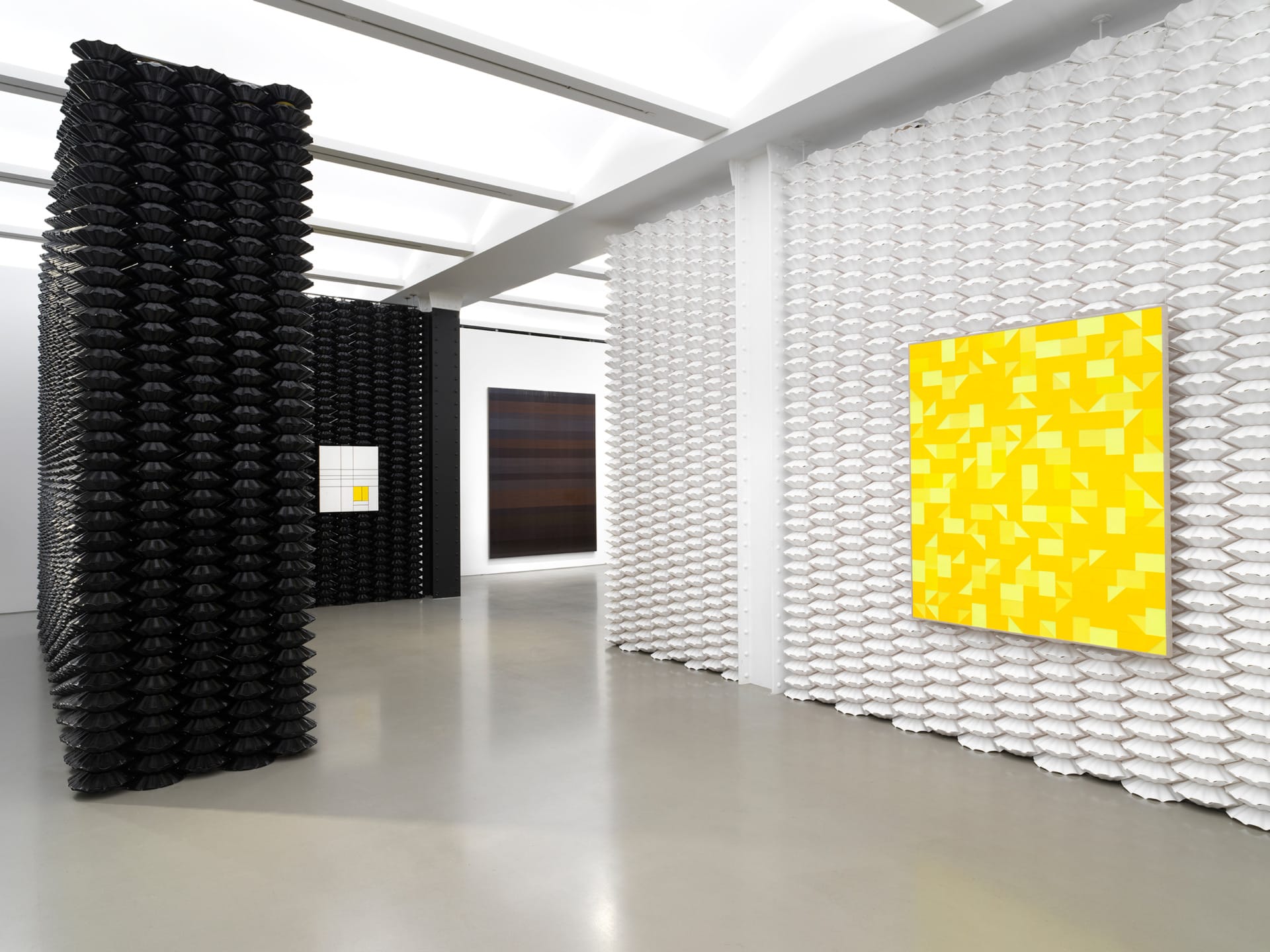 Contemporary art gallery with black and white sculptures and bright yellow geometric paintings on the walls.